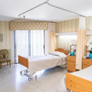 A well-lit hospital room featuring two adjustable beds separated by a privacy curtain.