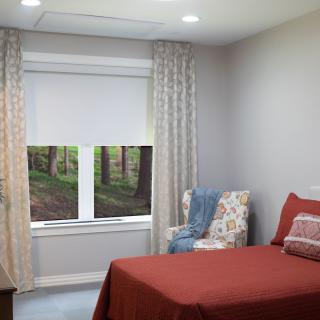 A cozy bedroom with a red bedspread and a floral armchair beside the window.