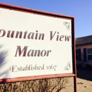 A sign for Mountain View Manor, established in 1967, with a building and clear sky in the background.