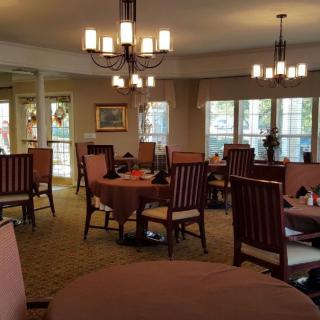 A cozy dining room with neatly arranged tables and chairs, illuminated by elegant chandeliers.