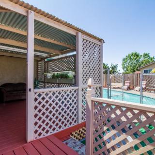 A cozy backyard setup featuring a covered patio with lattice walls and a fenced pool area.
