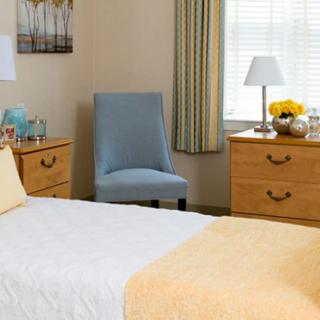 A cozy bedroom with two dressers, a blue chair, and a neatly made bed.