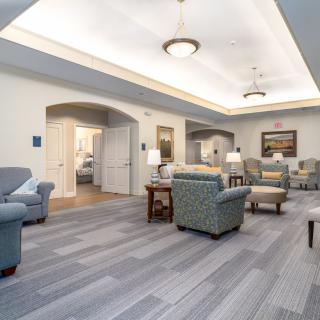 A spacious and elegantly designed living area featuring comfortable sofas and chairs, illuminated by ceiling lights.