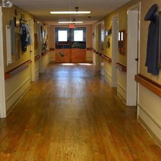 An empty hallway in a healthcare facility featuring wooden floors and double doors at the end.