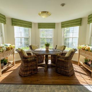 A cozy dining area with wicker chairs and a round table, bathed in natural light from multiple windows.