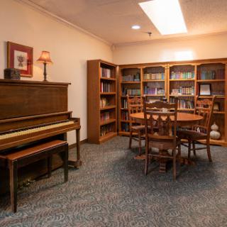 A cozy library space featuring a piano, bookshelves filled with books, and a dining table surrounded by chairs.