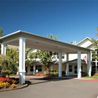 A well-maintained building entrance with a portico, surrounded by landscaped gardens on a sunny day.