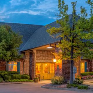 A warmly lit brick building surrounded by trees in the evening.