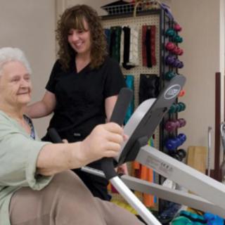 An elderly woman receiving guidance from a trainer during a physical therapy session.