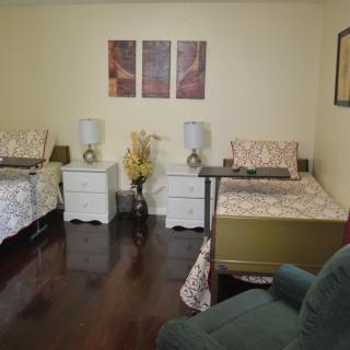 A cozy bedroom with two beds, nightstands, lamps, and artwork on the wall.