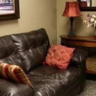 A cozy living room with a leather sofa, adorned with decorative pillows, next to a wooden side table and lamp.