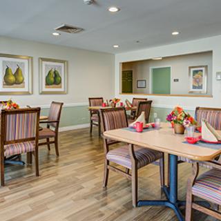 A cozy dining room with neatly arranged tables and chairs, featuring decorative wall art and a warm wooden floor.