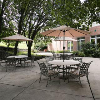 A serene outdoor patio area featuring tables and seating under large umbrellas, surrounded by lush greenery.