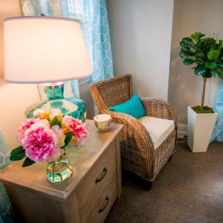 A cozy living room corner with a wicker chair, side table, and vibrant floral arrangement under soft lighting.