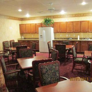 A cozy dining area with multiple tables and chairs, featuring a kitchenette with wooden cabinetry and a refrigerator.
