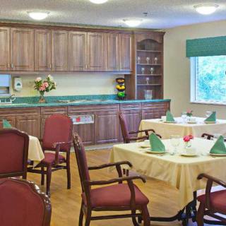 A neatly arranged dining area with tables, chairs, and a kitchenette in the background.