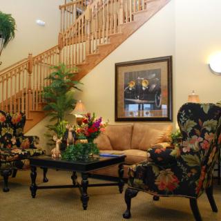 A cozy living room with floral chairs, a sofa, and a wooden staircase.