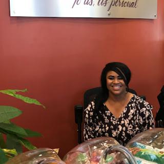 A cheerful person at a reception desk, surrounded by plants and decorative items.