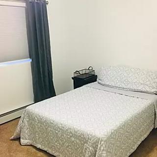 A minimalist bedroom with a neatly made bed, nightstand, and dark curtains.