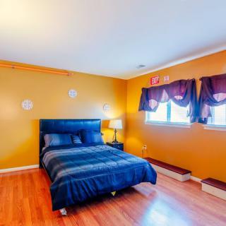 A cozy bedroom with vibrant orange walls and blue bedding, featuring wooden flooring and windows adorned with curtains.
