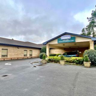 A view of the hotel entrance surrounded by well-maintained greenery under a cloudy sky.