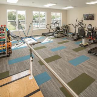 A well-lit gym with various fitness equipment including treadmills, ellipticals, and dumbbells.