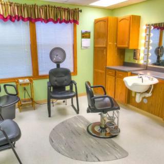A cozy hair salon interior featuring styling chairs, a dryer, and a sink with a mirror.