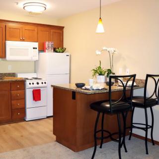 A cozy kitchen with wooden cabinets, a stove, refrigerator, and a small dining area.