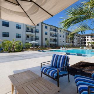 A sunny day at a modern apartment complex with a swimming pool and patio furniture.