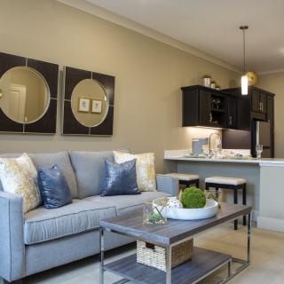 A cozy living room with a gray sofa, decorative pillows, a coffee table, and wall art adjacent to an open kitchen.