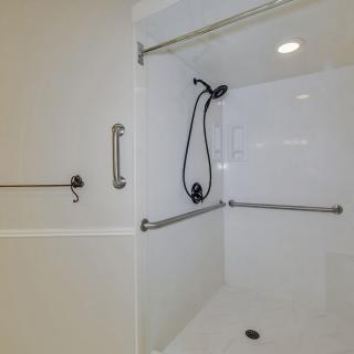 An accessible bathroom shower with grab bars and a handheld showerhead.