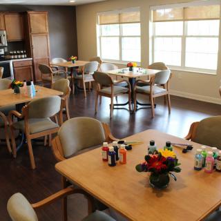 A communal dining and activity area with tables set up for arts and crafts, featuring paint supplies and flower centerpieces.