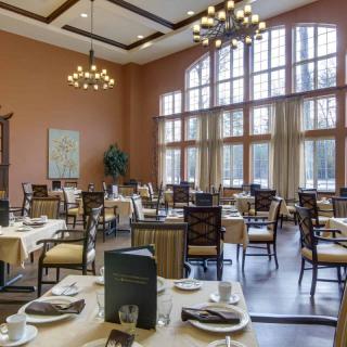 An elegant dining room with large windows and chandeliers, featuring neatly arranged tables.