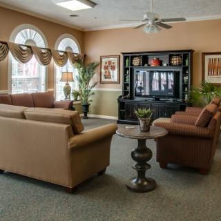 A cozy living room with sofas and a television, featuring large windows and tasteful decor.