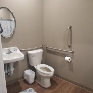 A clean bathroom with a toilet, sink, mirror, and handrails.