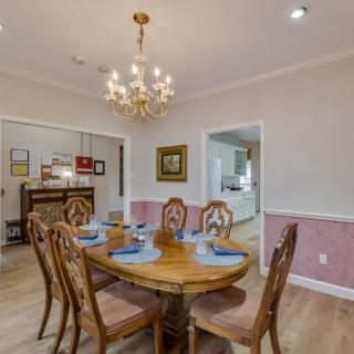 A cozy dining room with a wooden table set for six, featuring an elegant chandelier and tasteful wall art.
