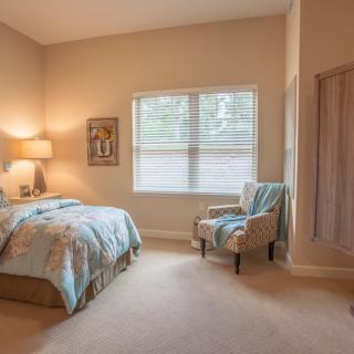 A cozy bedroom with a comfortable bed, a chair by the window, and soft lighting.