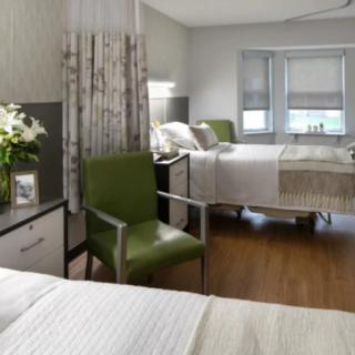 A clean and modern hospital room with two patient beds and comfortable seating.