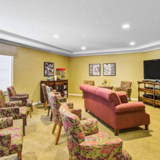A cozy living room featuring a sofa and several chairs arranged around a television, with decorative artwork on the walls.