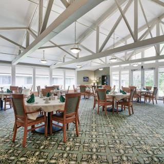A spacious dining room with neatly arranged tables and chairs, illuminated by natural light from large windows.