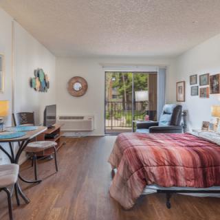 A cozy bedroom with a neatly made bed, wall art, and a view of the outdoors through a large window.