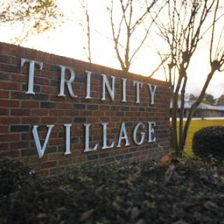 Entrance sign of Trinity Village, showcasing the name against a natural backdrop.