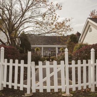 A quaint house with a white picket fence surrounded by autumn foliage.