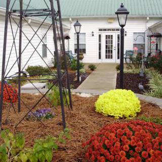 A beautifully landscaped garden with colorful flowers, lamp posts, and a small windmill structure in front of a building.