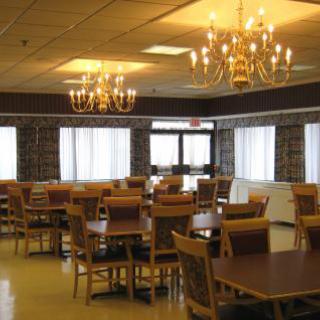 A well-lit dining room with multiple tables and chairs, featuring elegant chandeliers and large windows.