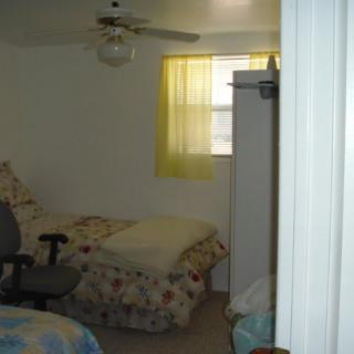 A small bedroom with a bed, chair, and a window with yellow curtains.