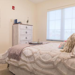 A cozy bedroom with a bed, dresser, and a large window.