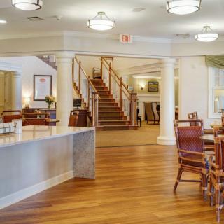 A spacious lobby area with wooden flooring and elegant furniture, featuring a staircase and bright lighting.