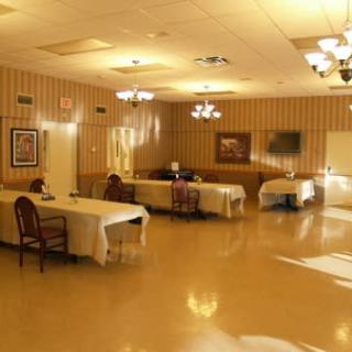 An empty dining area with tables and chairs, featuring chandeliers and wall art.