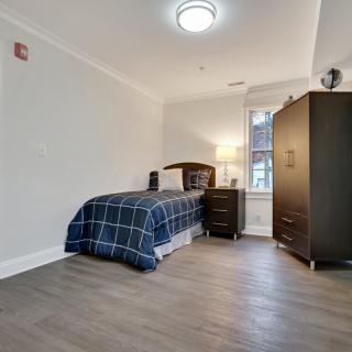 A minimalist bedroom with a single bed, wardrobe, and lamp.